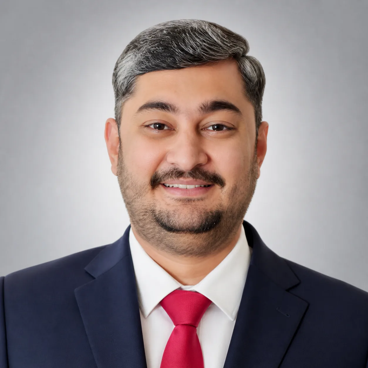 Head-and-shoulders portrait of a smiling man in a navy suit and red tie against a gray backdrop.