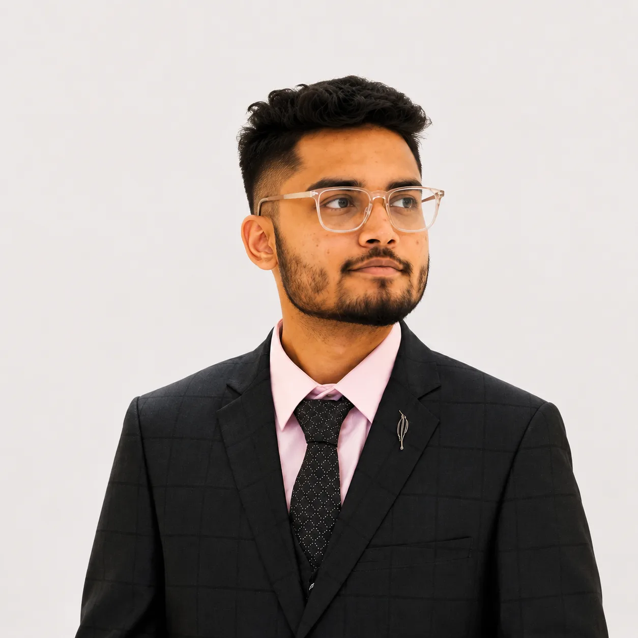 Portrait of a man with glasses wearing a dark plaid suit and pink shirt, looking to the side.